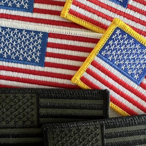 May include: Four embroidered American flag patches, two with yellow borders and two with black borders. The patches are arranged in a stack.