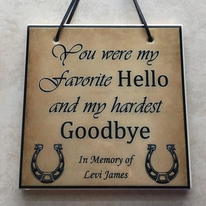 May include: A brown and white ceramic plaque with black text and two black horseshoes. The text reads "You were my favorite hello and my hardest goodbye. In memory of Levi James."