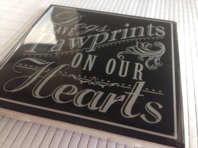 May include: Black and white sign with the text "Dogs leave paw prints on our hearts".