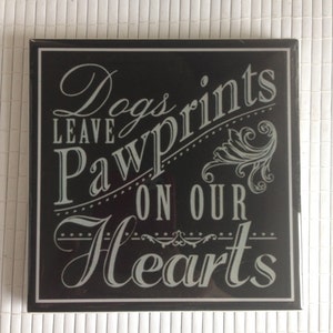 May include: Black and white sign with the text "Dogs leave paw prints on our hearts".
