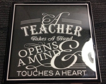 May include: A black and white square tile with the text "A Teacher Takes A Hand Opens A Mind & Touches A Heart".