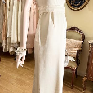 May include: A white sleeveless maxi dress with a beaded neckline and a fitted bodice. The dress has a simple, elegant design and is perfect for a formal occasion.
