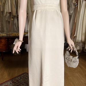 May include: A sleeveless white satin dress with a beaded neckline and a matching sash. The dress has a simple, elegant design and is perfect for a formal occasion.