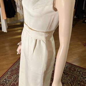 May include: A white sleeveless dress with a beaded neckline and a fitted silhouette. The dress has a belt at the waist and a straight skirt.