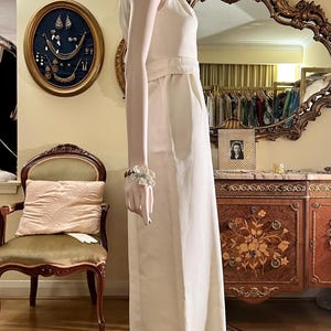 May include: A white sleeveless jumpsuit with a V-neckline and a wide leg. The jumpsuit is made of a lightweight fabric and has a relaxed fit. The model is wearing a silver headband.