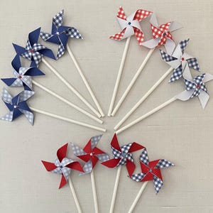May include: A set of ten red, white, and blue pinwheels with white sticks. The pinwheels have a gingham pattern and are perfect for a summer party or celebration.