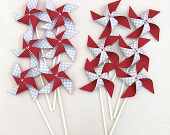 May include: A collection of eight pinwheels arranged in two groups. Each pinwheel features alternating blades of solid red cardstock and light blue and white gingham patterned paper, all mounted on thin white sticks with a small center fastener.