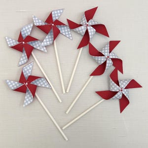 May include: Five pinwheels arranged in a fan shape, each featuring four alternating blades of solid red cardstock and light blue and white gingham patterned paper, all attached to thin white sticks with a small center fastener.