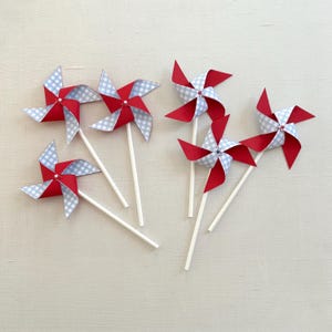 May include: Six red and blue gingham paper pinwheels with white sticks. The pinwheels have a red and white gingham pattern on one side and a blue and white gingham pattern on the other side.
