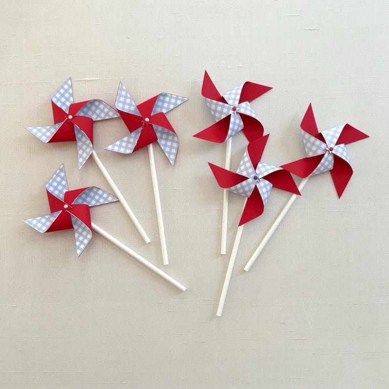 May include: Six red and blue gingham paper pinwheels with white sticks. The pinwheels have a red and white gingham pattern on one side and a blue and white gingham pattern on the other side.