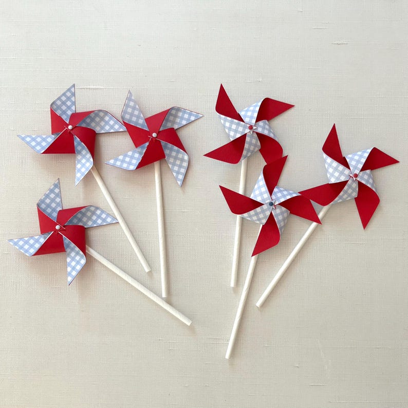 May include: Six red and blue gingham paper pinwheels with white sticks. The pinwheels have a white dot in the center.