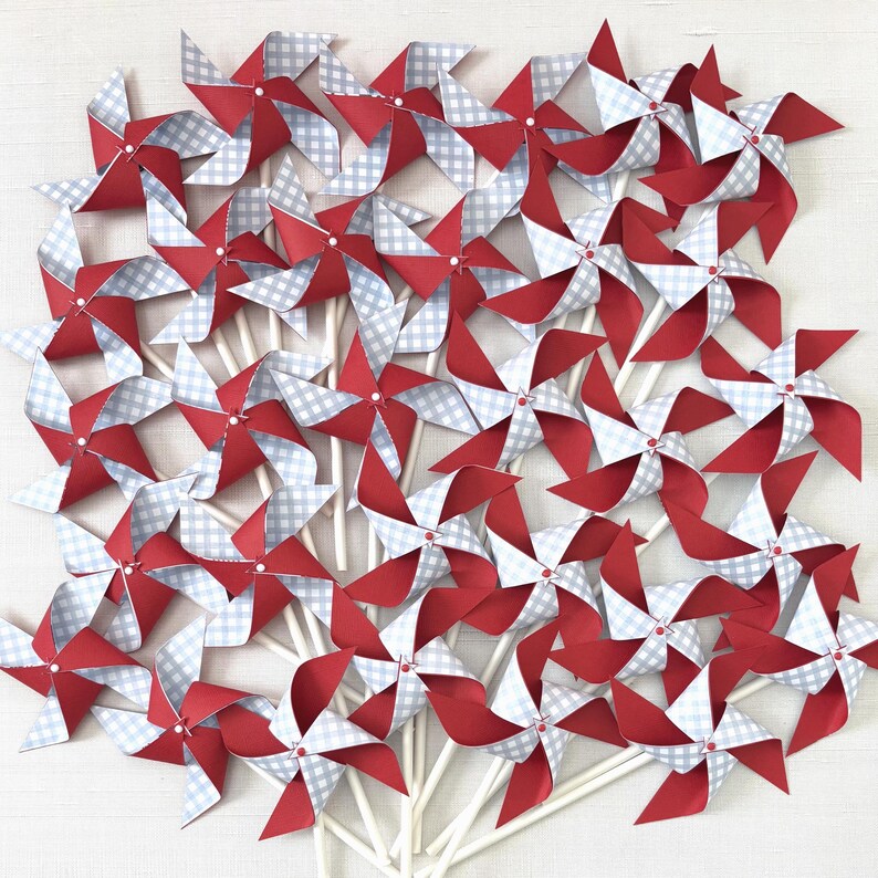 May include: A collection of numerous paper pinwheels arranged in a cluster. Each pinwheel features four blades with alternating solid red and light blue and white gingham checkered patterns, all attached to thin white sticks at the center.