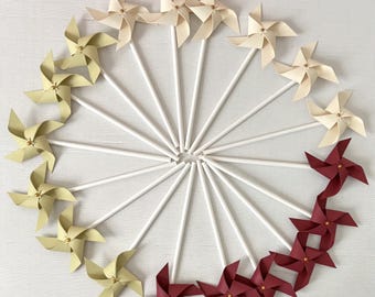 13 docenas de mini molinillos de viento giratorios en color verde salvia dorado, vino tinto y beige cremoso con remaches centrales dorados.