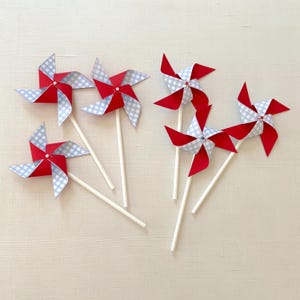 May include: Six red and blue pinwheels with white sticks. The pinwheels have a gingham pattern and are attached to white sticks.