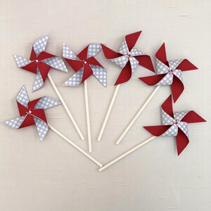 May include: Five pinwheels arranged in a fan shape, each featuring four alternating blades of solid red cardstock and white and light gray gingham patterned paper. Each pinwheel is attached to a thin, white, cylindrical paper stick.