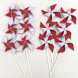 May include: A collection of eight pinwheels arranged in two groups, each featuring a four-pointed design with alternating solid red and light blue gingham patterned paper blades attached to thin white sticks with a small white center fastener.
