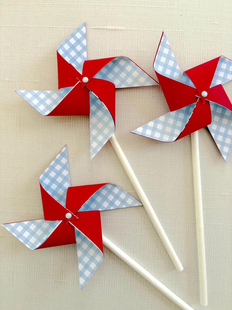 May include: Three red and blue pinwheels with white gingham patterns on the blades. The pinwheels are attached to white sticks.