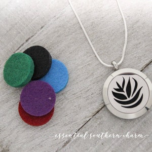 May include: A silver necklace with a round pendant featuring a black leaf design. The pendant has a removable top to insert essential oil pads. Five colorful felt pads are included: green, black, blue, purple, and red.