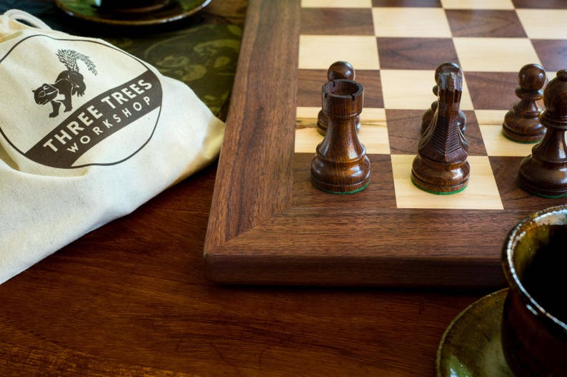 Close up of corner of walnut and maple chess board with solid walnut border, and wooden chess pieces set up to play.