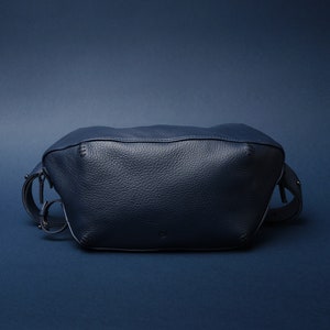 May include: A dark blue leather fanny pack with a zipper closure and a buckle strap.