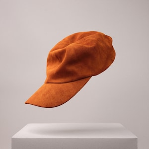 May include: A brown suede baseball cap with a curved brim. The cap is floating above a white platform.