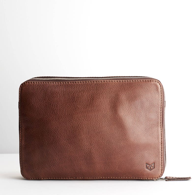 May include: A brown leather zippered pouch with a small logo on the bottom right corner.