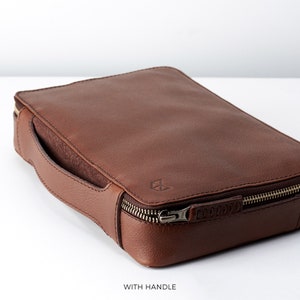 May include: A brown leather zippered pouch with a handle. The pouch has a small logo embossed on the front.