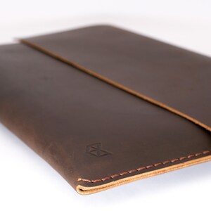 May include: A brown leather laptop sleeve with a stitched edge and a small logo on the front.