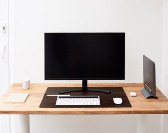 Op de afbeelding: Een houten bureau met een zwarte computermonitor, een wit toetsenbord, een witte muis, een witte beker, een notitieboekje en een zwarte laptop op een standaard.