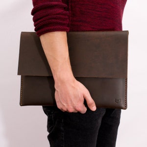 May include: A brown leather laptop sleeve with a flap closure and a small logo on the front.