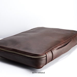 May include: A brown leather laptop case with a zipper closure and a top handle.  The case is made of high-quality leather and has a sleek, professional design.