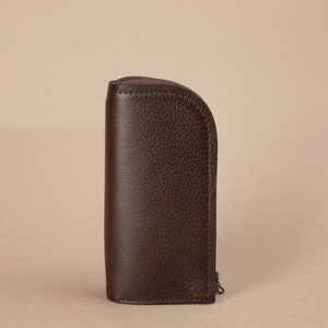 Puede incluir: Una bolsa de cuero marr&oacute;n con cremallera y acabado texturizado.