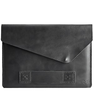 Könnte beinhalten: Schwarze Lederhülle für Laptops mit Klappenverschluss und einem Riemen mit Nähten. Die Hülle hat ein kleines Logo in der unteren rechten Ecke.