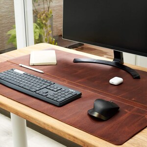 May include: A brown leather desk mat with a black keyboard, a white wireless mouse, and a white notebook on a wooden desk.