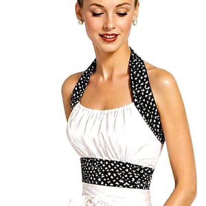 May include: A white halter dress with a black and white polka dot pattern on the halter top and waist. The dress has a full skirt and a bow at the waist. A black and white polka dot bracelet is on the wrist.