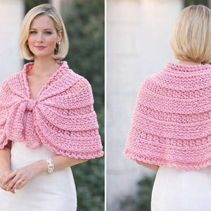 May include: A light pink, crocheted shawl with a bow closure. The shawl is made of a chunky yarn and has a scalloped edge. The image shows the shawl from the front and back.