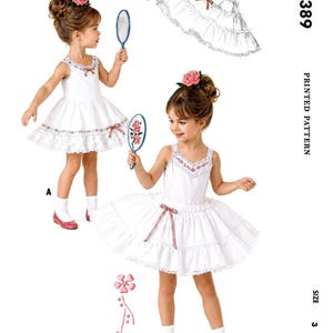 Puede incluir: Un patrón impreso para un enagua y una enagua de niña. La imagen muestra a una niña pequeña con un vestido blanco con adornos de encaje, un lazo rosa y una flor a juego en el pelo. El texto "CHILD'S SLIPS AND PETTICOAT" está en la parte superior.