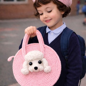 May include: A pink crocheted round handbag featuring a white poodle design. The bag has a matching pink handle and a small tail detail. A matching pink beret with a pom-pom is also visible.