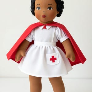 May include: A handmade doll dressed as a nurse, wearing a white uniform with a red cross on the pocket, a red cape, and a white cap with a red cross. The doll has brown skin, black hair, and white shoes with red bows. The text "413-T" is in the upper left.