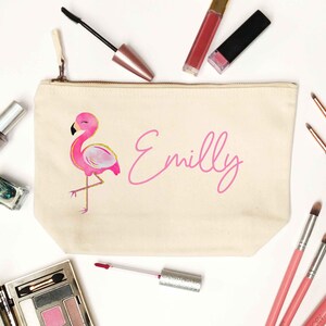 May include: A cream canvas makeup bag featuring a pink flamingo design and the name "Emilly" in pink script. The bag is surrounded by makeup brushes, lipsticks, and eyeshadow.