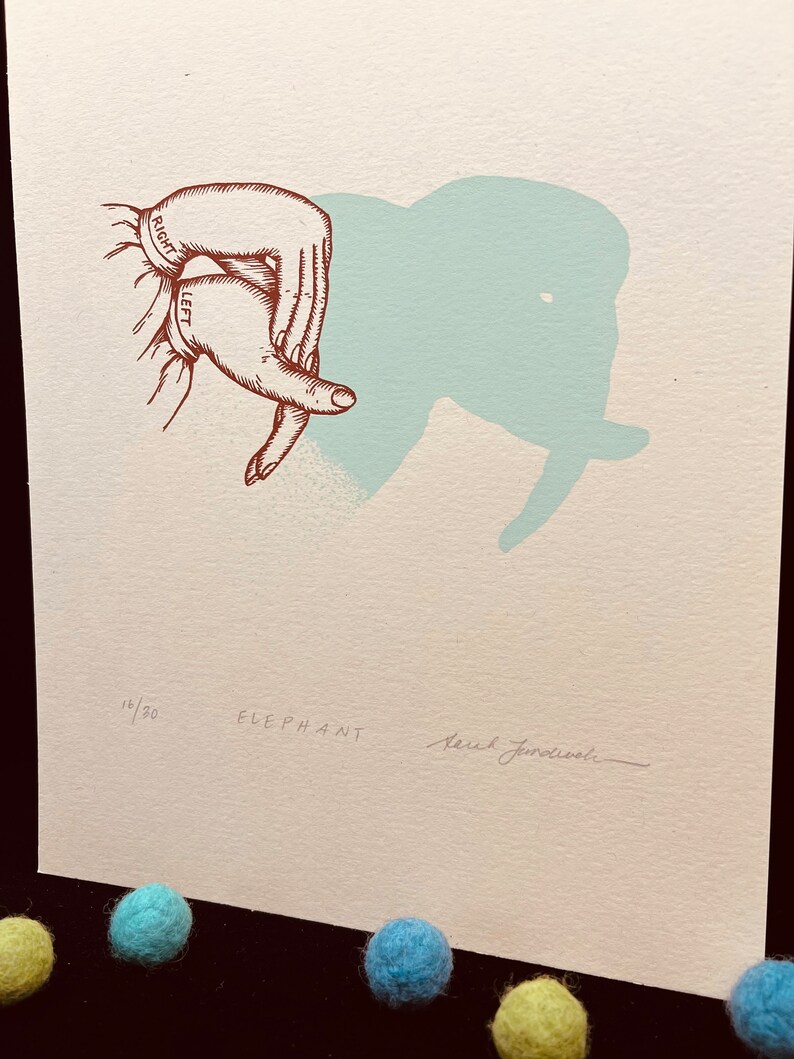 May include: A hand shadow art print with a light blue elephant silhouette. The print is numbered 18/30 and signed "Sarah Janecowski".