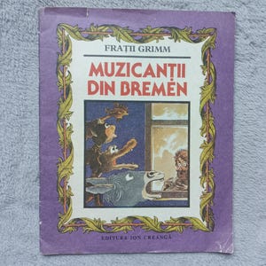 May include: A paperback book titled Frații Grimm Muzicanții din Bremen with a purple cover featuring a yellow leaf border. The central illustration depicts a donkey, dog, cat, and rooster looking through a window at a person. Editura Ion Creangă.