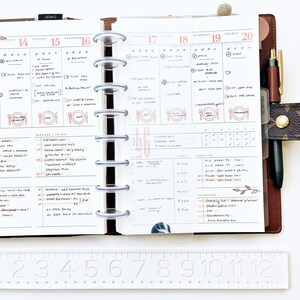 Peut inclure: Un agenda hebdomadaire avec une couverture en cuir marron et un reliure &agrave; anneaux argent&eacute;s. L'agenda a une mise en page quotidienne avec des sections pour les objectifs, les courses, les vitamines, les pas, la cr&eacute;ativit&eacute; et les arriv&eacute;es. L'agenda est ouvert &agrave; la semaine du 14 juillet au 20 juillet.