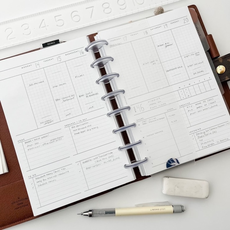 Peut inclure: Un planneur blanc ouvert sur une semaine, avec une couverture en cuir marron. Le planneur est ouvert sur une semaine avec des notes manuscrites et des listes de choses &agrave; faire. Le planneur est dot&eacute; d'un syst&egrave;me de reliure &agrave; disques en plastique transparent.