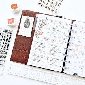 Peut inclure: Un planneur blanc ouvert sur la semaine du jeudi 14 ao&ucirc;t au mercredi 17 ao&ucirc;t. Le planneur pr&eacute;sente un motif floral et des notes manuscrites. Il est dot&eacute; d'une couverture en plastique transparent et d'un reliure &agrave; anneaux argent&eacute;s.