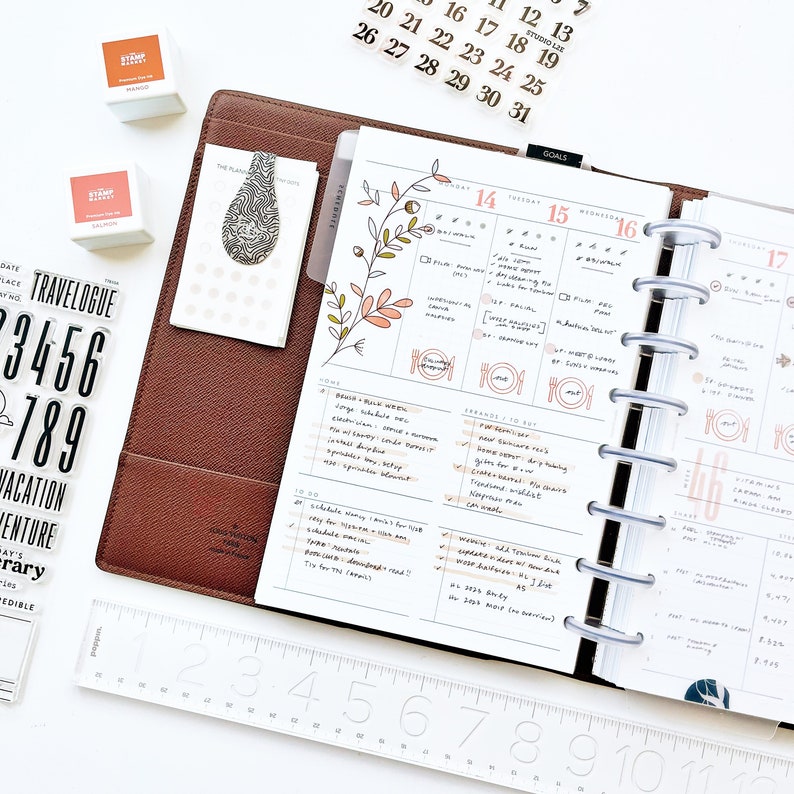 Peut inclure: Un planneur blanc ouvert sur la semaine du jeudi 14 ao&ucirc;t au mercredi 17 ao&ucirc;t. Le planneur pr&eacute;sente un motif floral et des notes manuscrites. Il est dot&eacute; d'une couverture en plastique transparent et d'un reliure &agrave; anneaux argent&eacute;s.