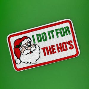 Peut inclure: Écusson brodé représentant le Père Noël avec le texte "I DO IT FOR THE HO'S" en vert et rouge. L'écusson a un fond blanc avec une bordure rouge et un fond vert.