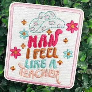 May include: Embroidered patch featuring a pink, white and blue cloud design and the text "How I feel like a teacher" in a colourful font. The patch is surrounded by a pink border and features small embroidered flowers.
