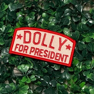 May include: A red and white embroidered patch with the text "*DOLLY FOR PRESIDENT*" in white lettering.