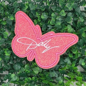 May include: Pink glitter butterfly patch with the word "Dolly" embroidered in white.